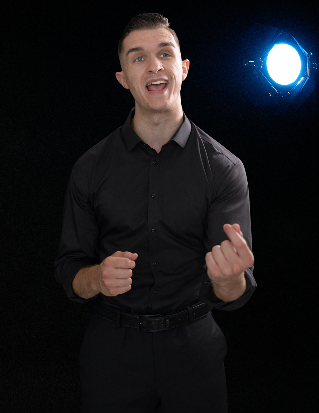 Man in black shirt gestures, smiling, with glowing blue light behind him.