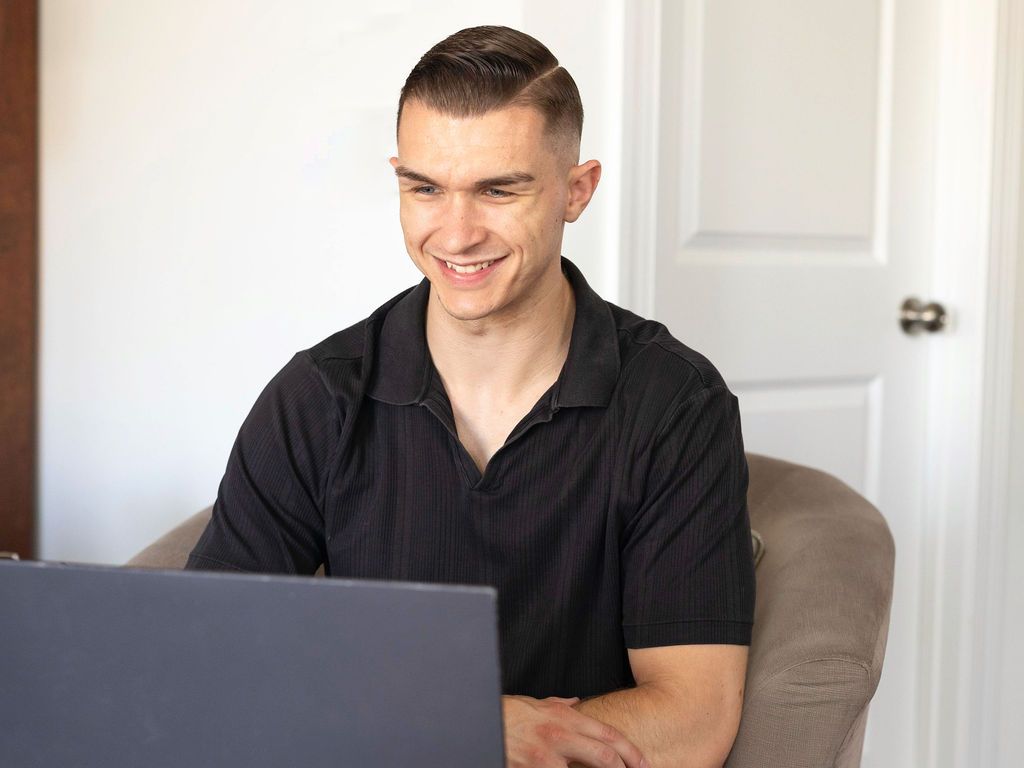 Man smiling while working on a laptop in a bright room