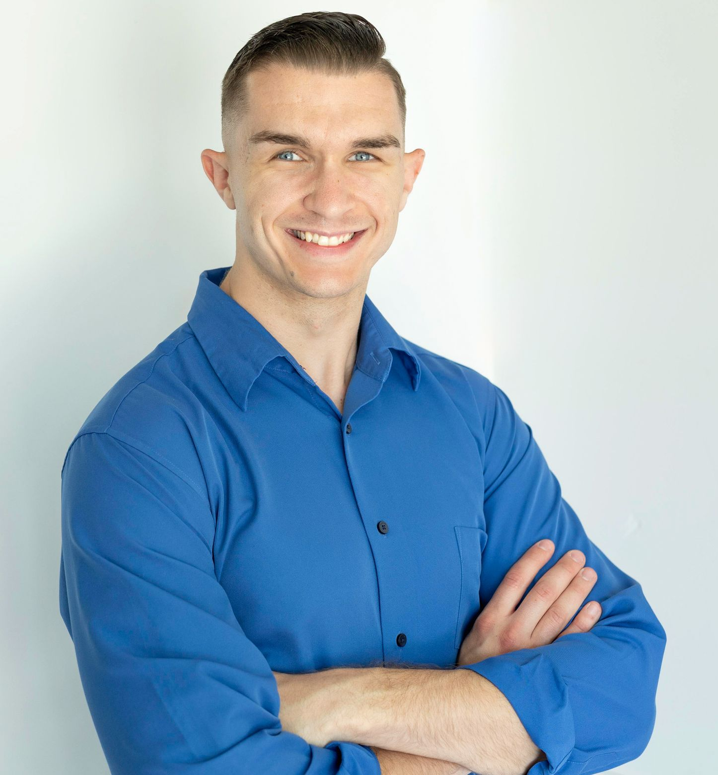 Smiling person in a blue button-up shirt with arms crossed against a light background