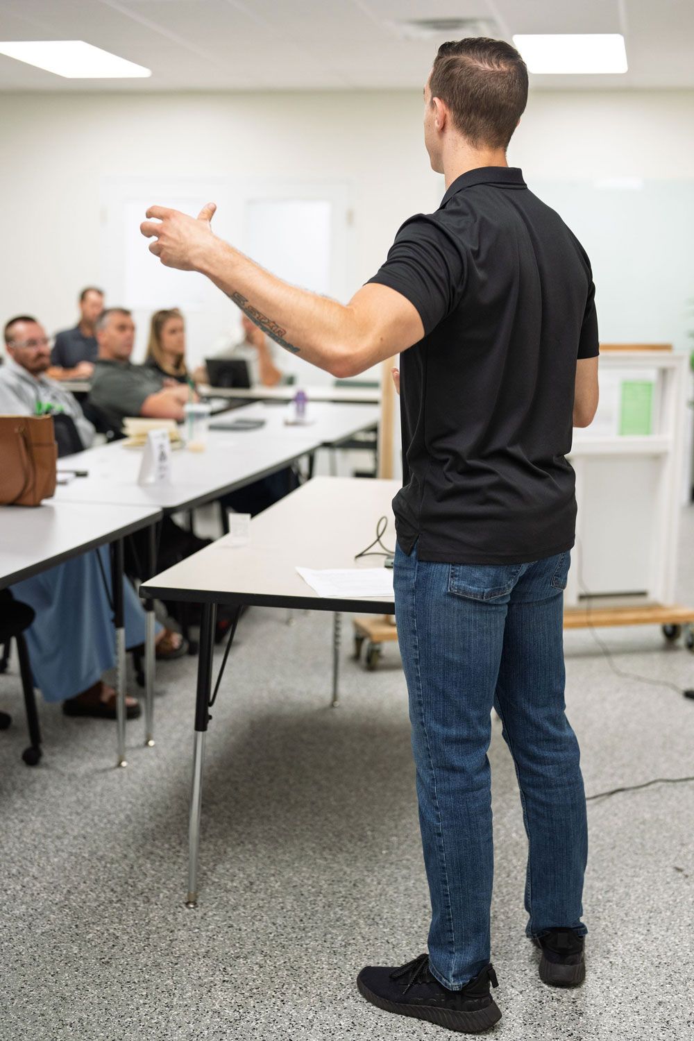 Man presenting to a seated classroom audience in a bright meeting room
