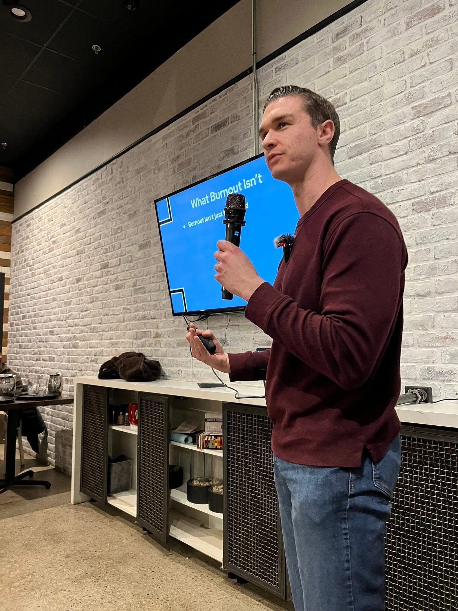 Speaker holding a microphone and remote in front of a blue presentation screen indoors