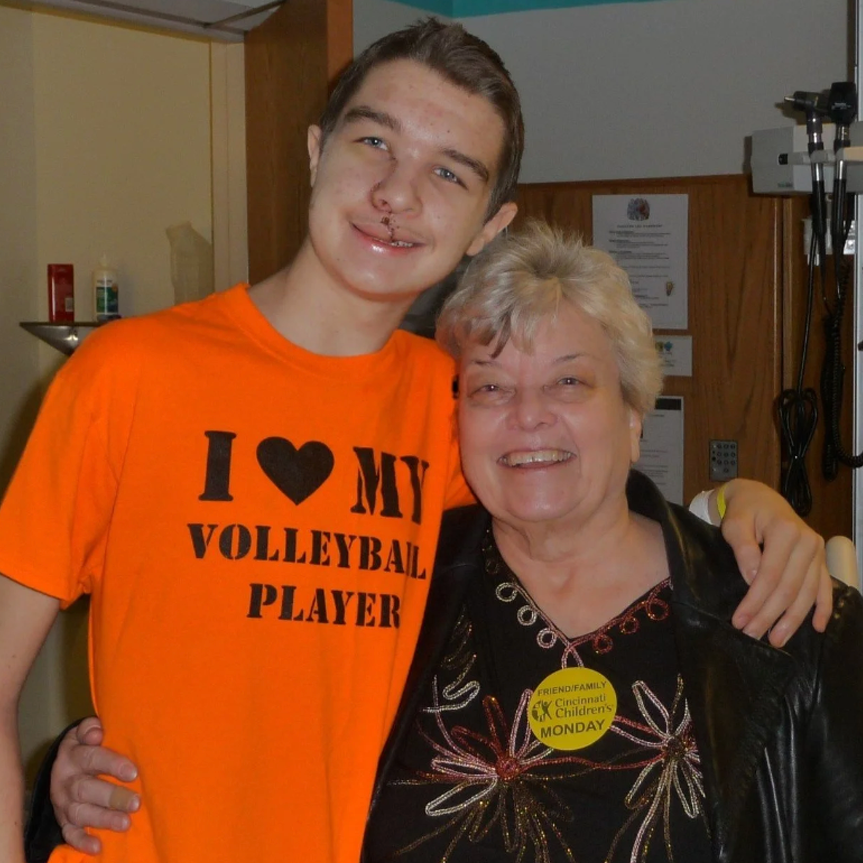 Man in orange shirt hugs woman; both smile. The shirt says 