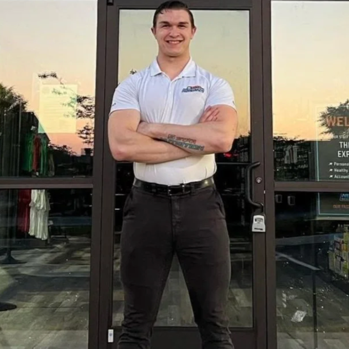 Man in white shirt and dark pants, arms crossed, standing in front of glass doors.