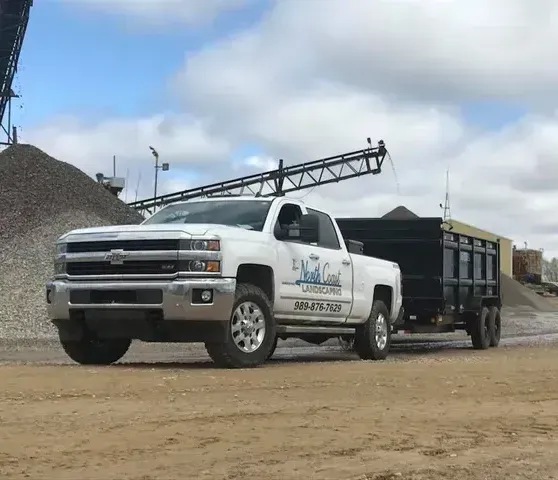 A white truck with a black trailer is parked in a dirt lot.