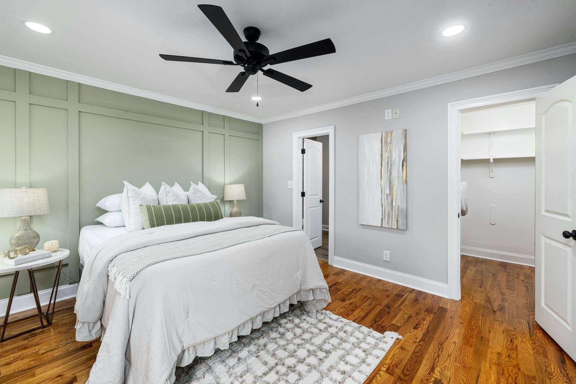 Bedroom with a light green accent wall, white bedding, wooden floor, and a black ceiling fan.