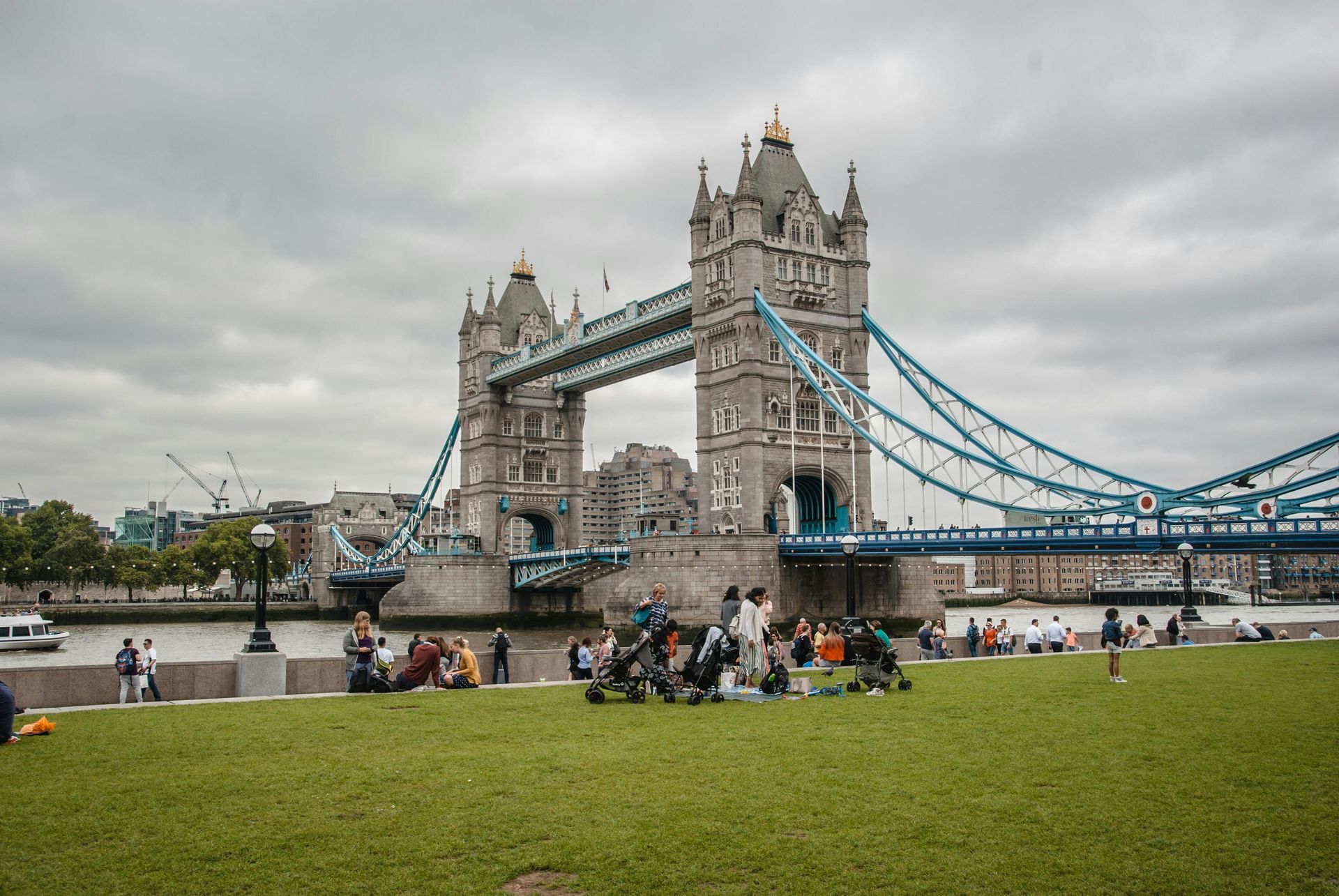 Tower Bridge over the Thames with people on the riverbank under a cloudy sky