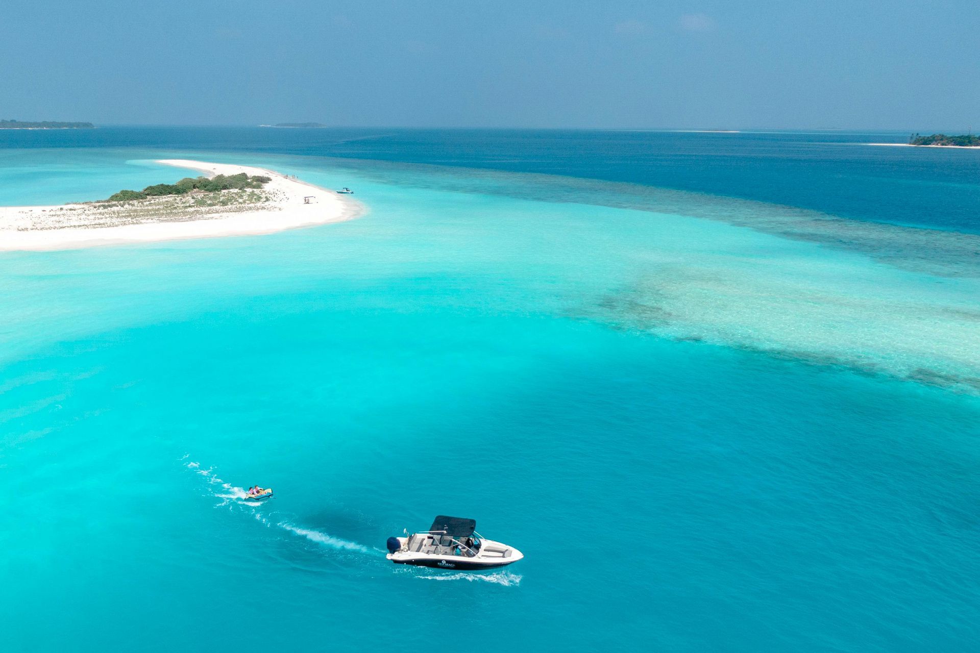 Small motorboat on bright turquoise water near a sandy island under clear blue sky