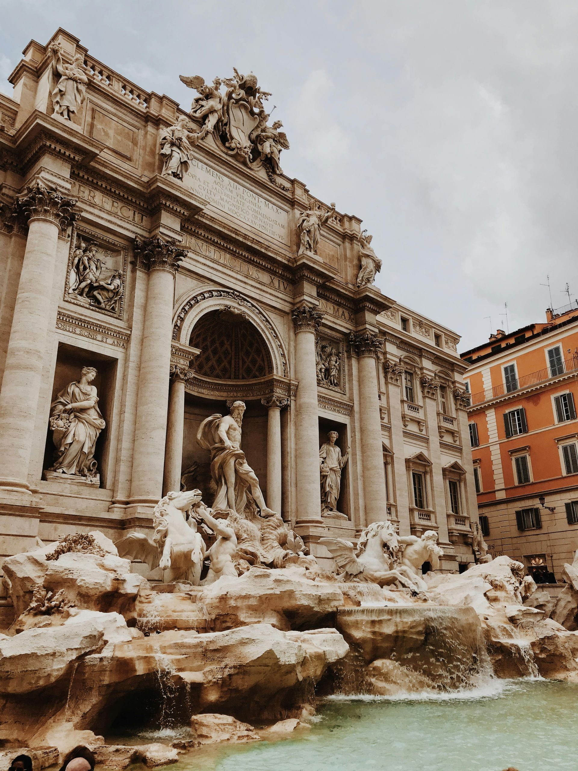 Trevi Fountain in Rome with ornate marble statues and turquoise water under a cloudy sky