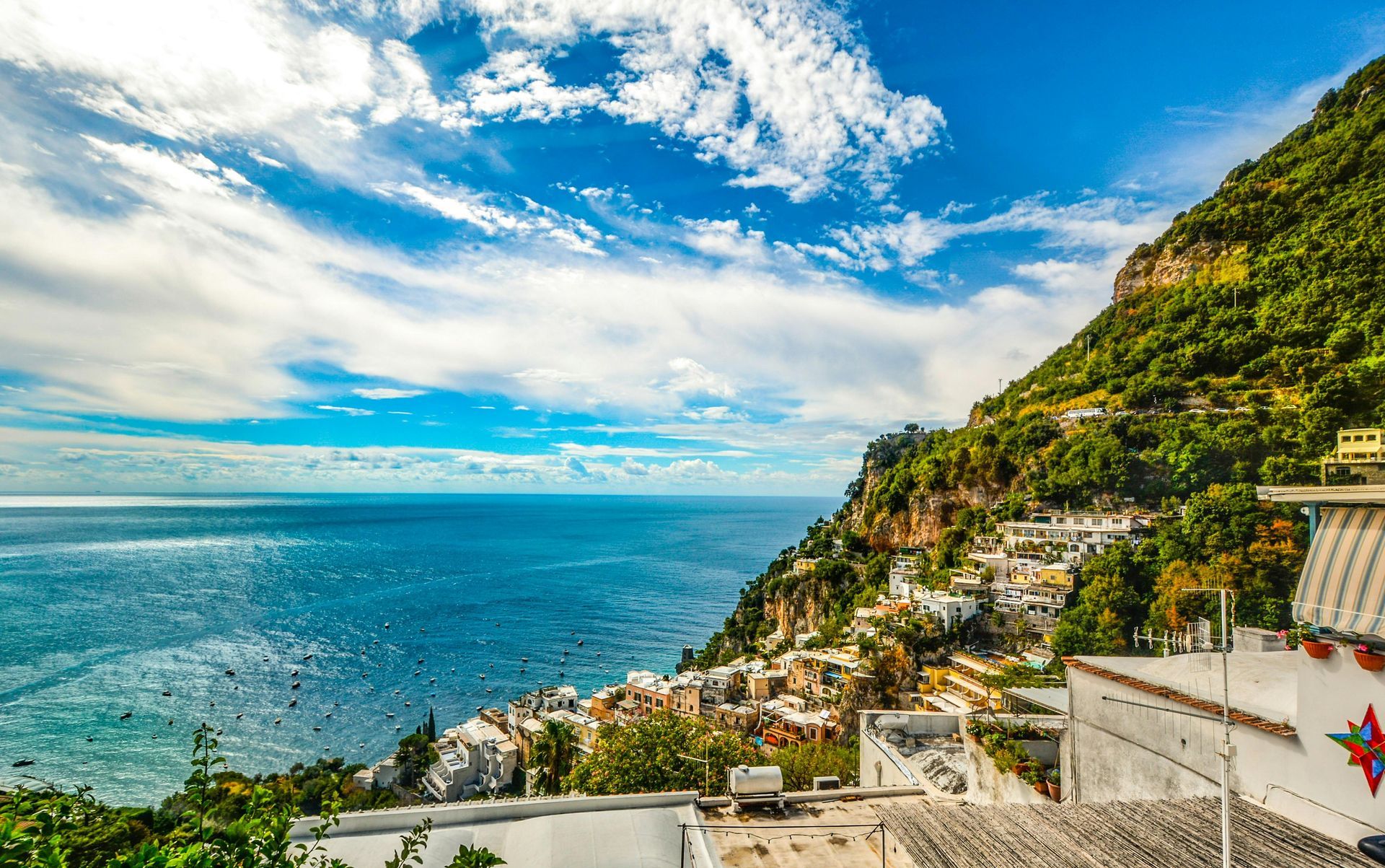 Coastal hillside town overlooking a bright blue sea under a partly cloudy sky