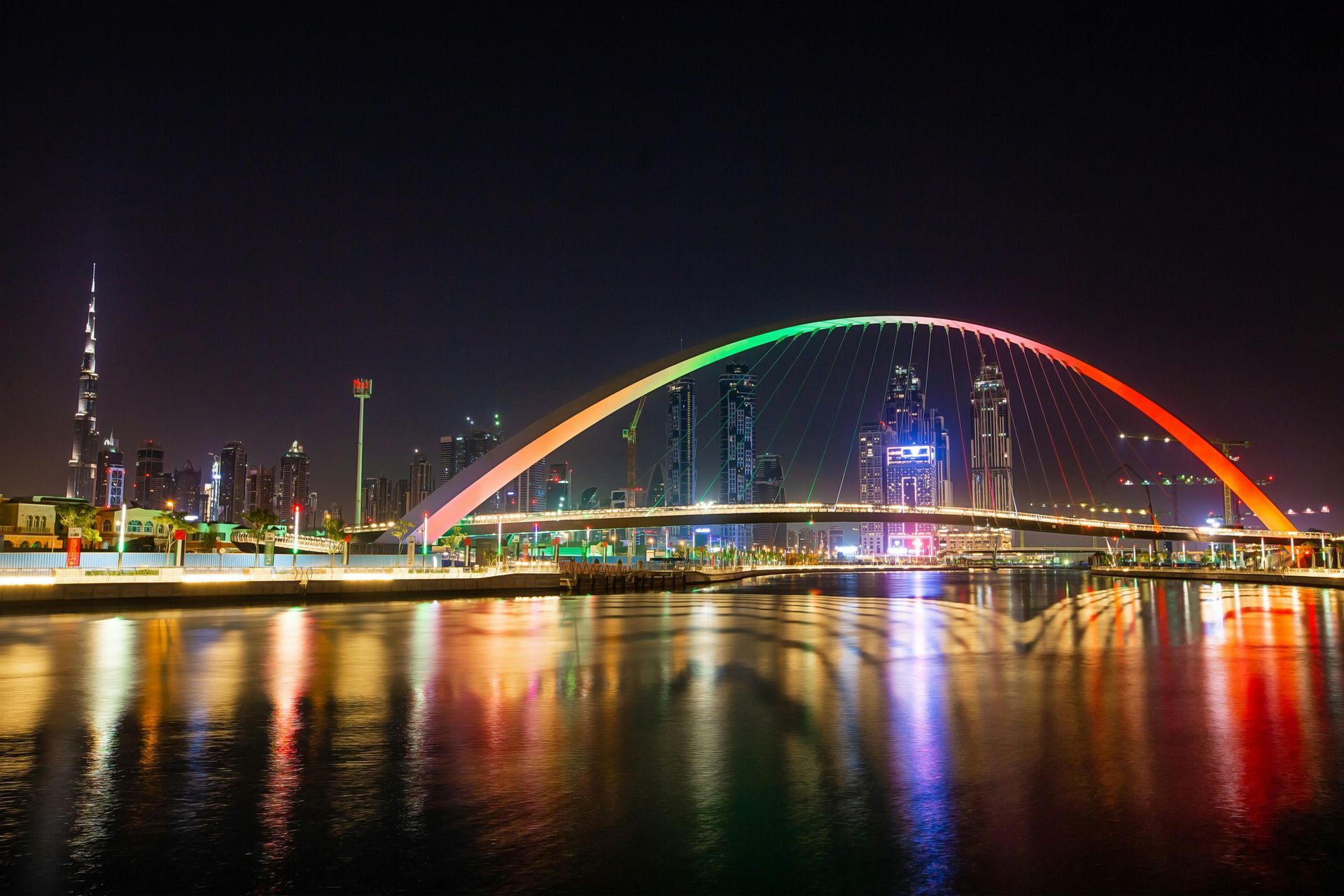 Night skyline with a rainbow-lit arched bridge reflecting on the water