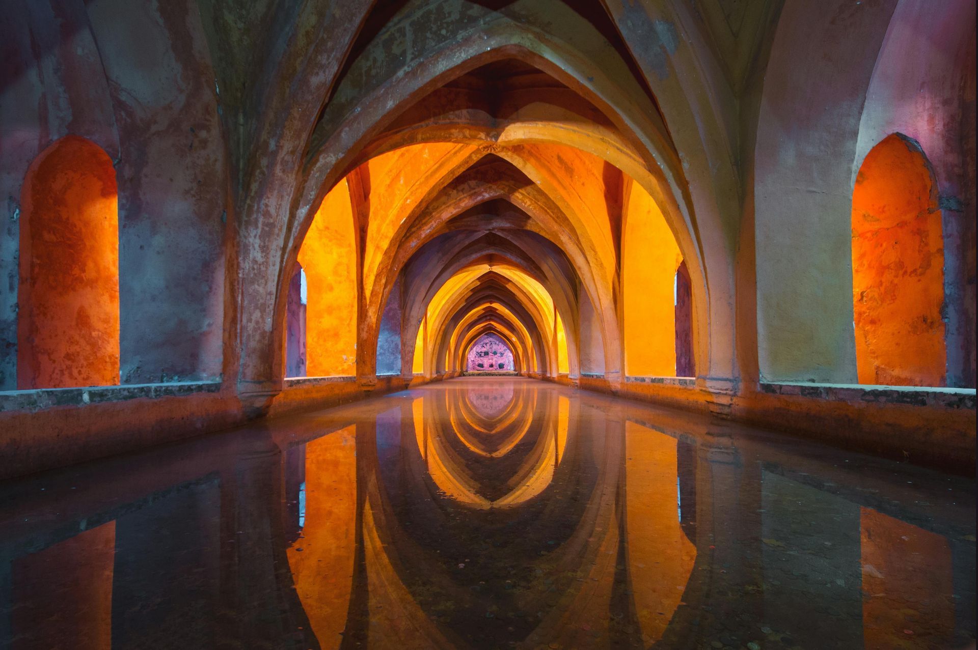 Symmetrical arched tunnel with warm orange light and reflections in calm water