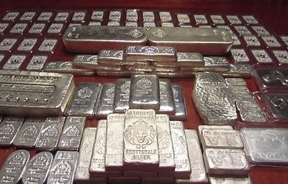 Assorted silver bullion bars and ingots stacked in rows on a red surface