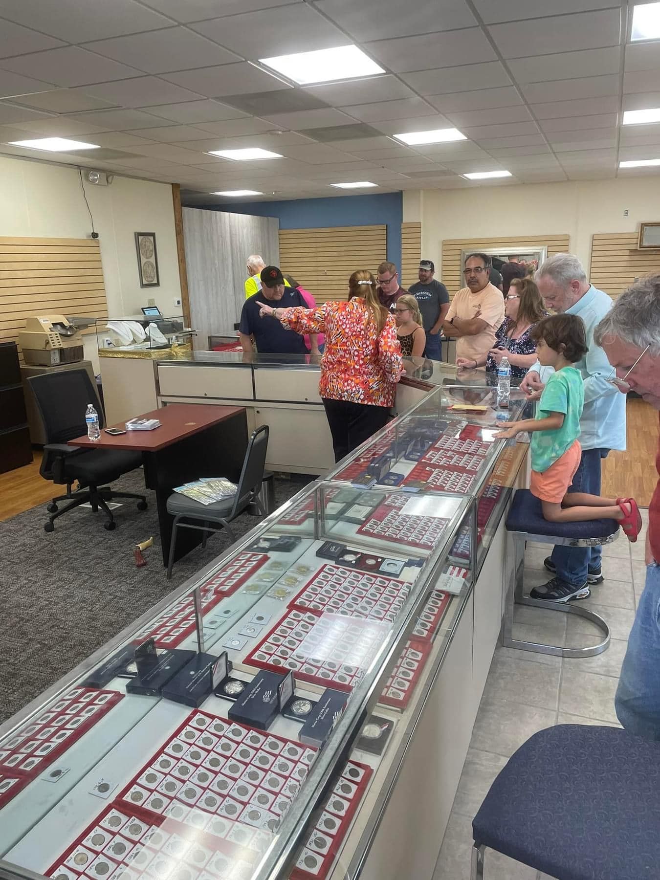 People browsing jewelry at a long display table in a bright indoor shop room