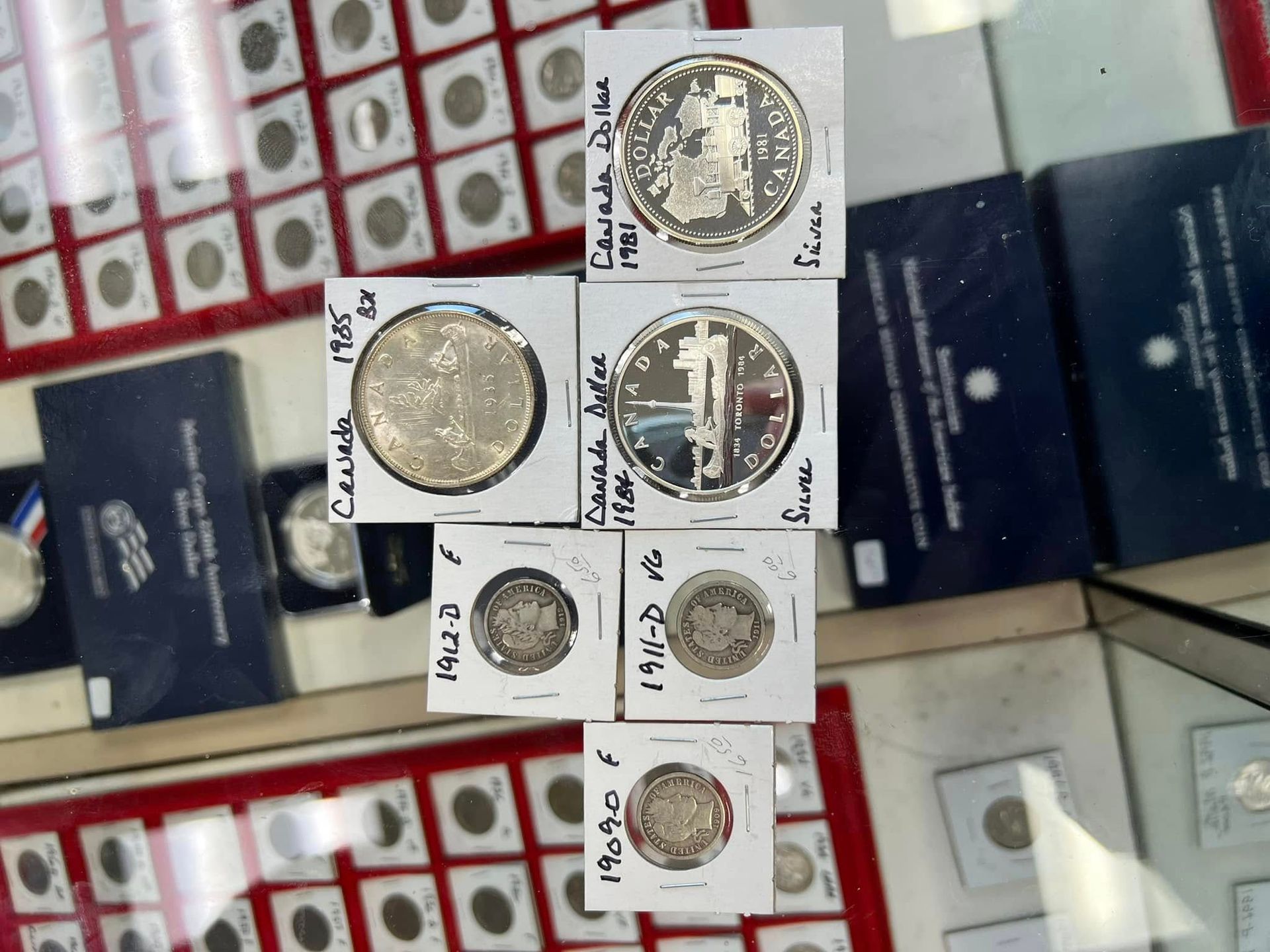 Display of assorted coins on white cards in a shop window, with dark blue boxes and red coin trays behind them.