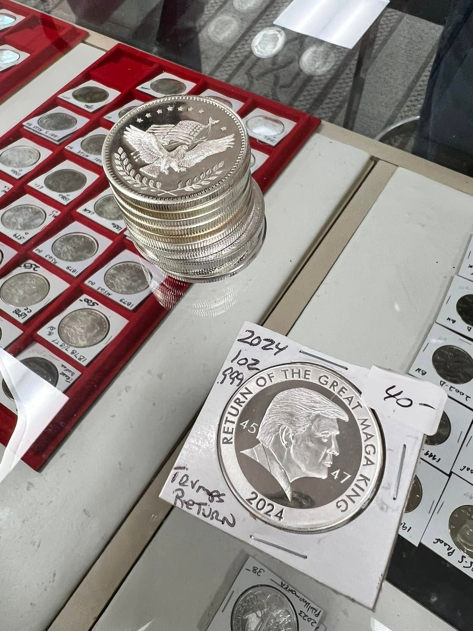 Stack of silver coins and coin holders on a glass display case with red-lined trays.