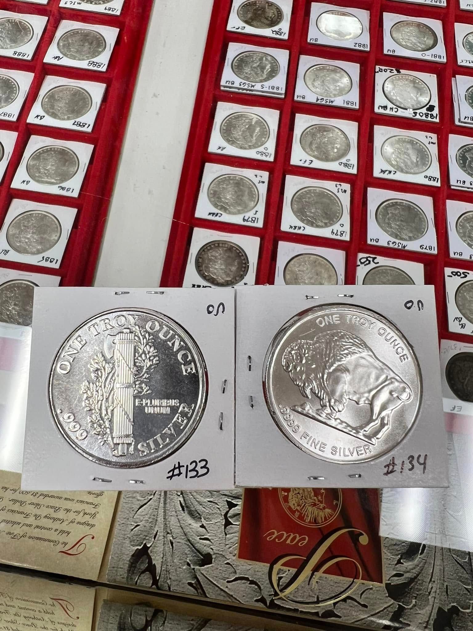 Silver coin shown in two views on a white card, with many coin trays in the background.
