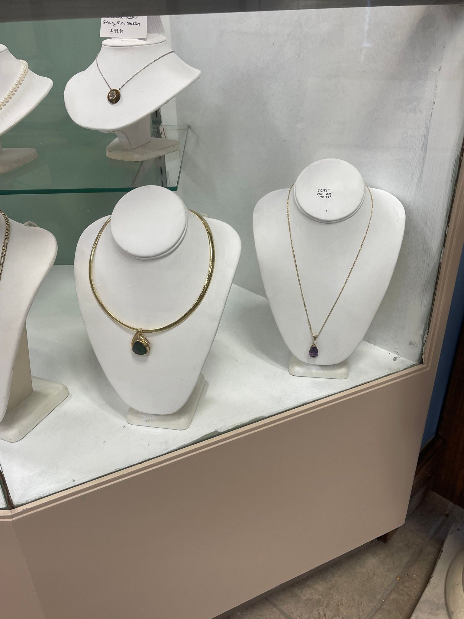 Jewelry store display with white busts showing gold and silver necklaces in a glass case