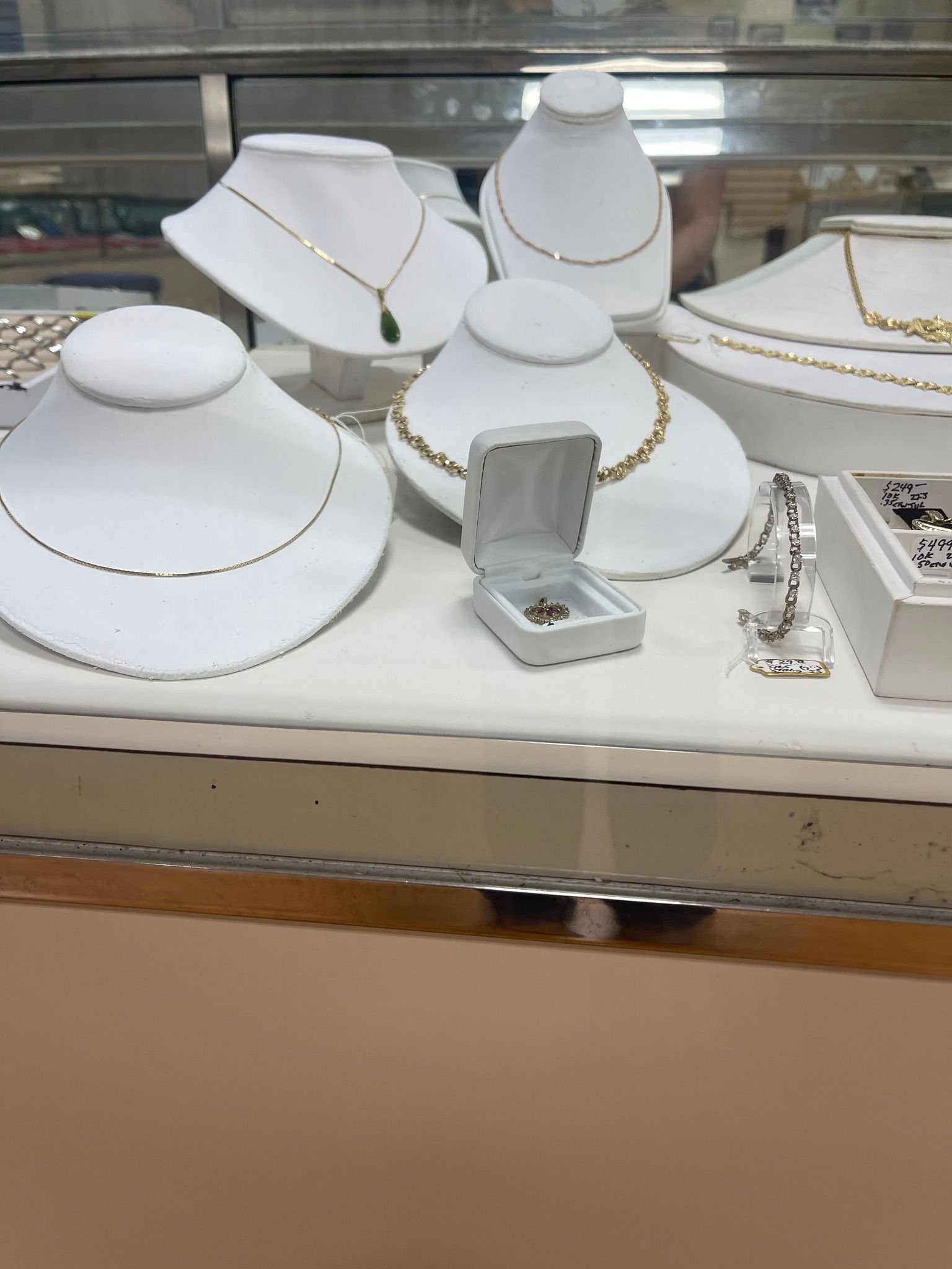 White jewelry busts and trays displaying gold necklaces and rings in a store case