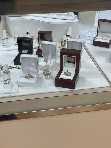 Assorted rings in display boxes on a jewelry store shelf, mostly white and burgundy cases.