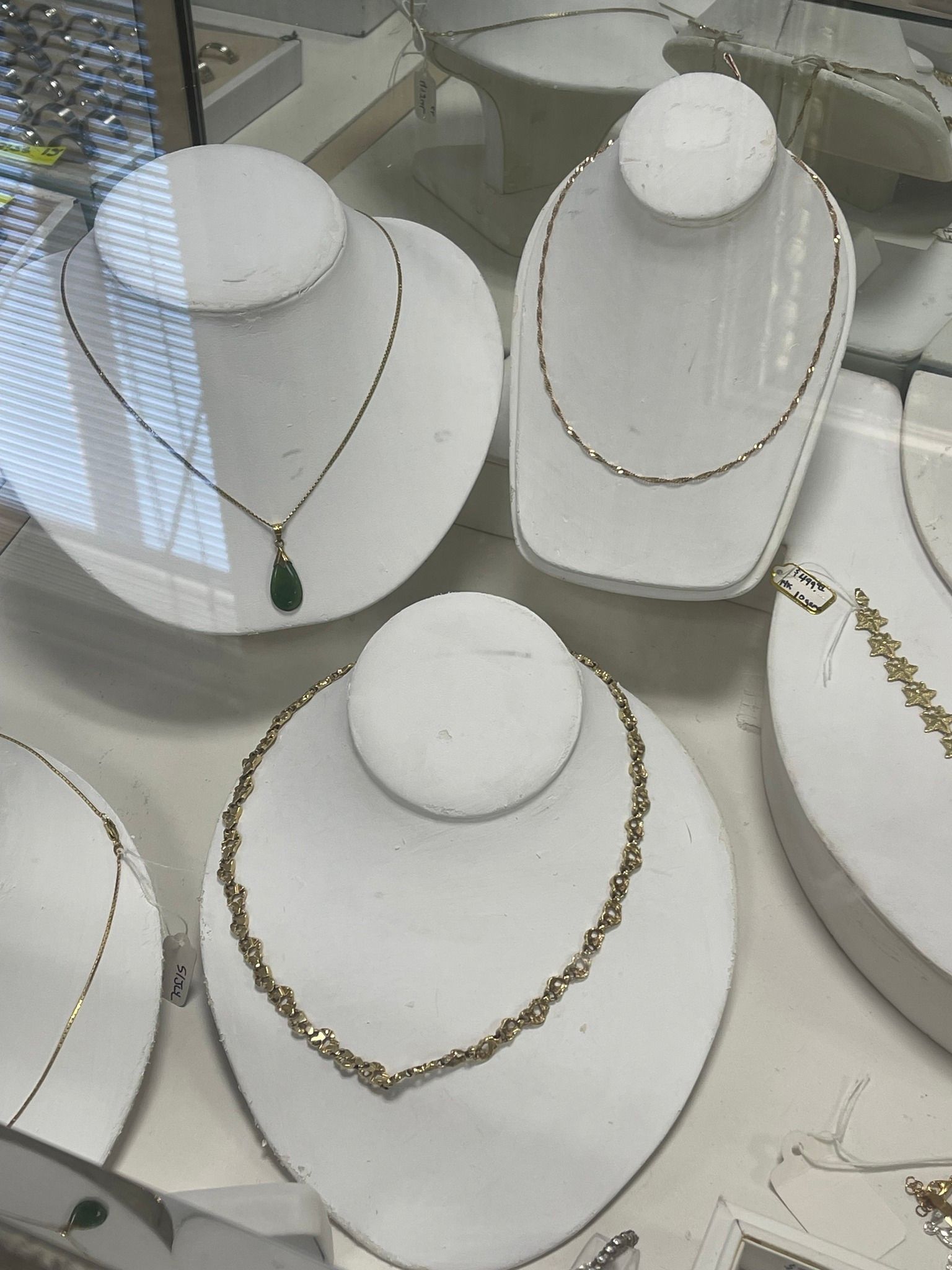 White necklace display stands in a jewelry shop, with gold and green necklaces on several busts.