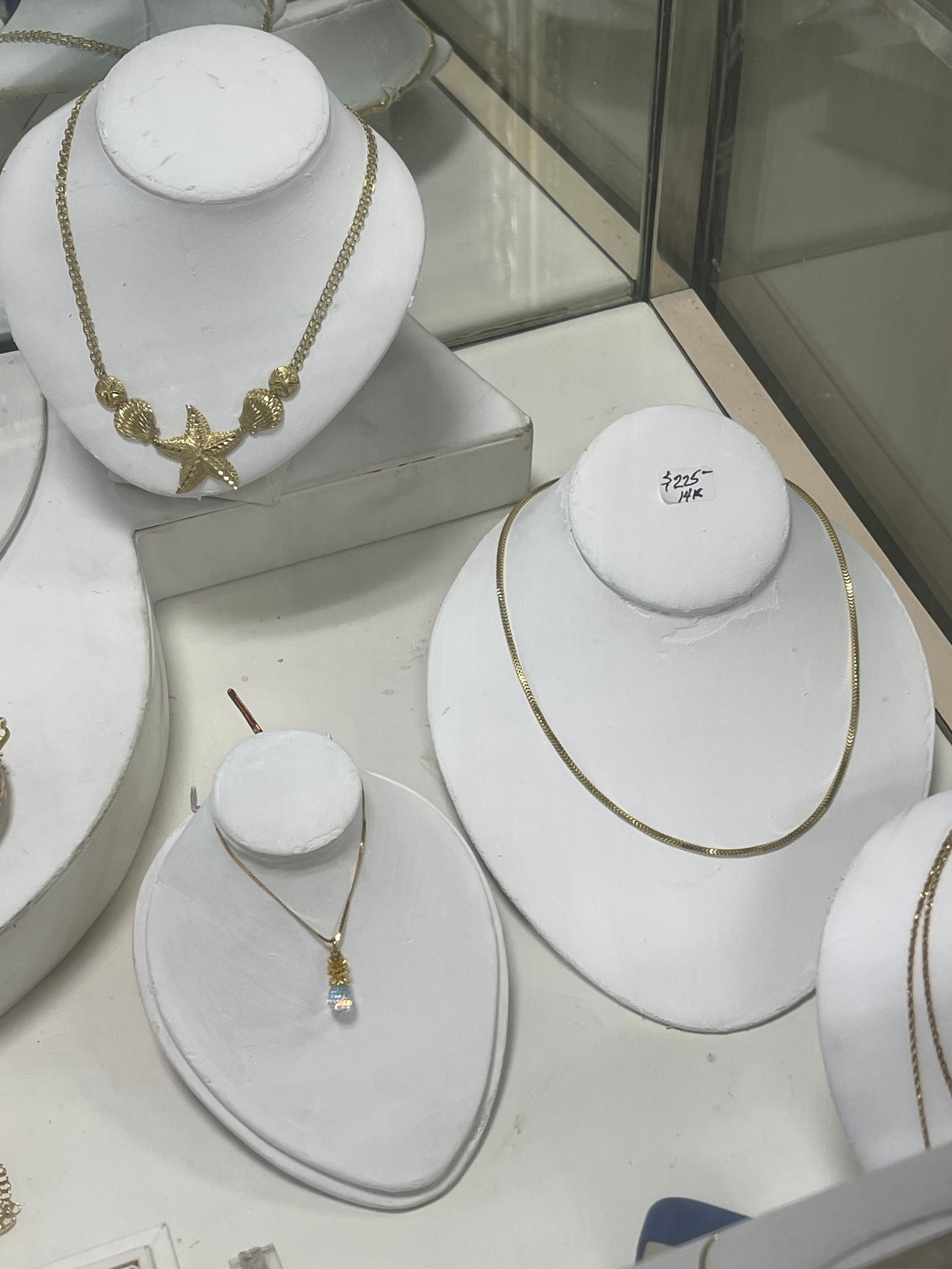 Jewelry display case with gold necklaces on white bust stands and a silver necklace on a gray stand