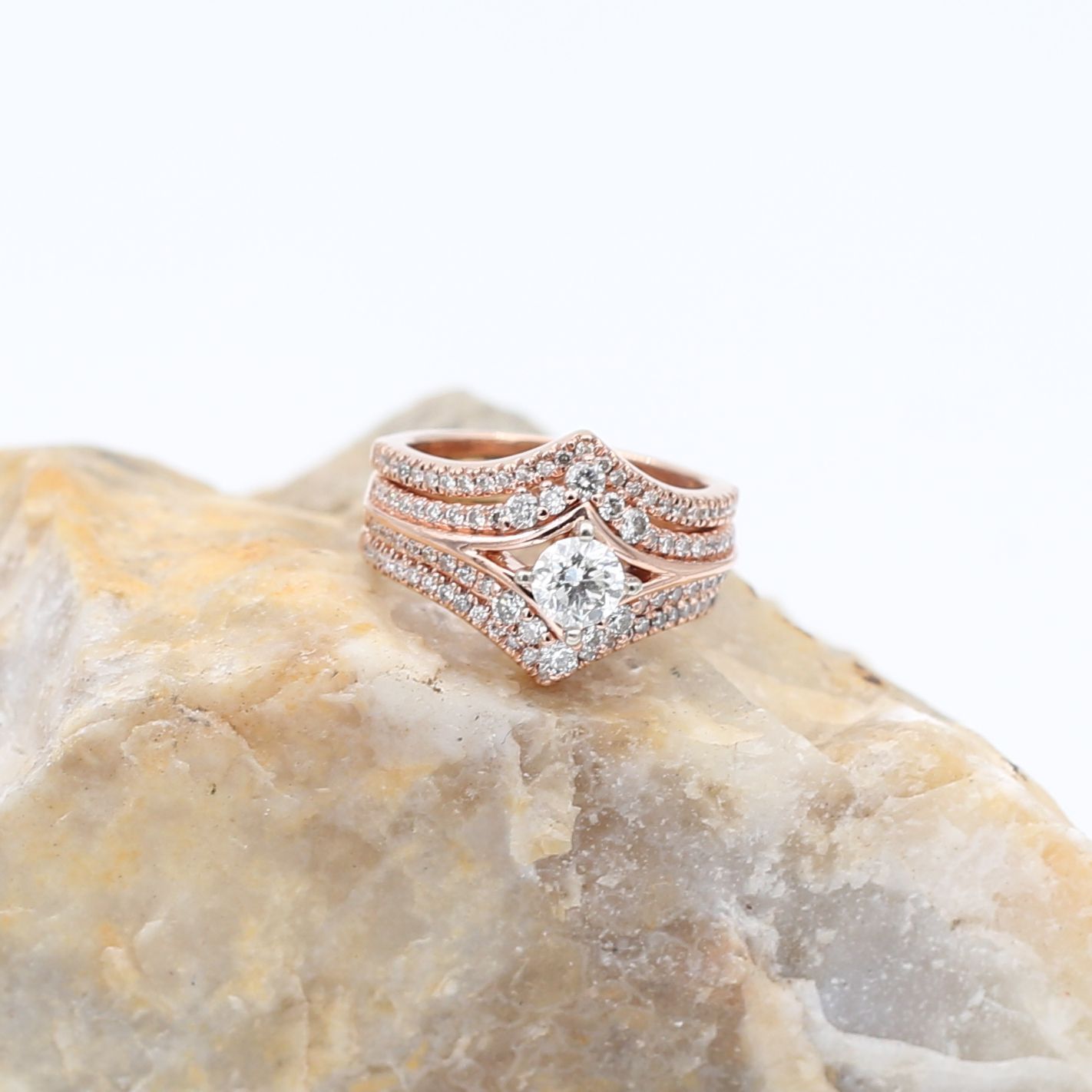 Rose gold diamond ring set on a pale stone against a white background