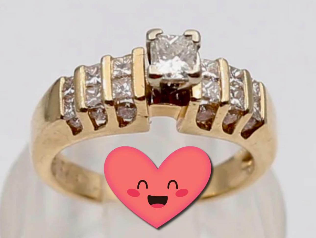 Gold ring with five clear gemstones, one larger center stone and a pink heart overlay below it