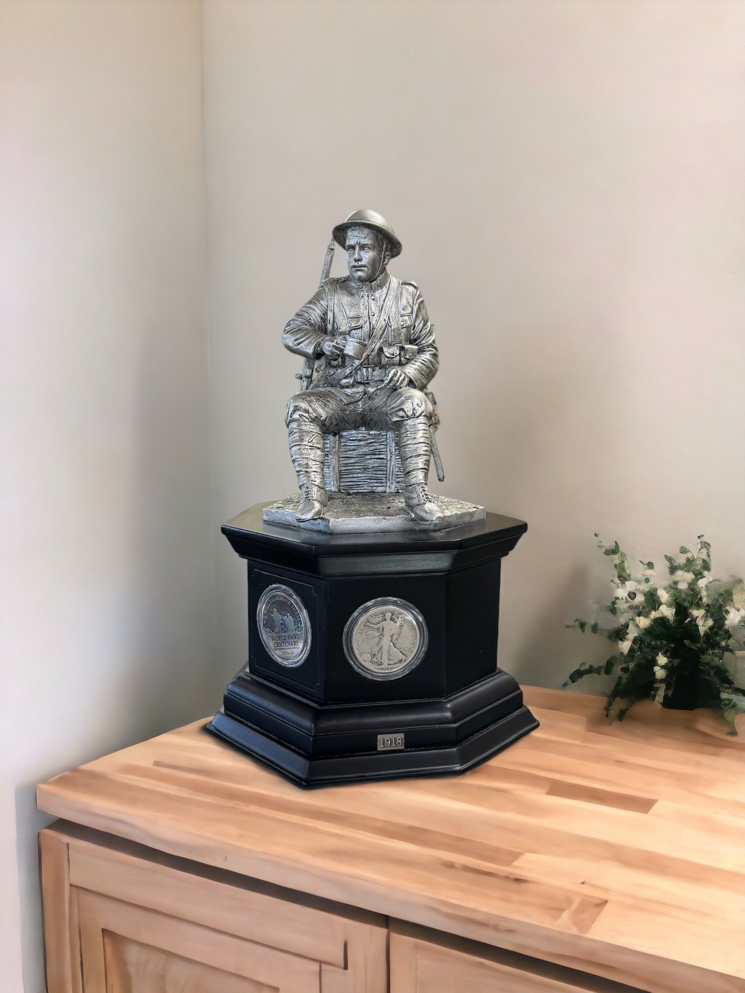 Decorative silver figurine on a black pedestal atop a wooden cabinet beside flowers in a corner nook