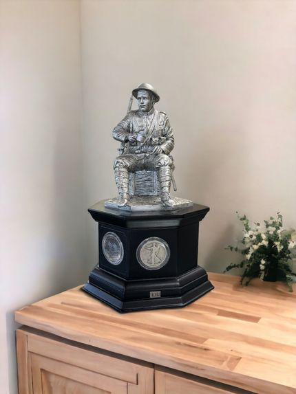 Decorative silver figurine on a black pedestal atop a wooden cabinet beside flowers in a corner nook