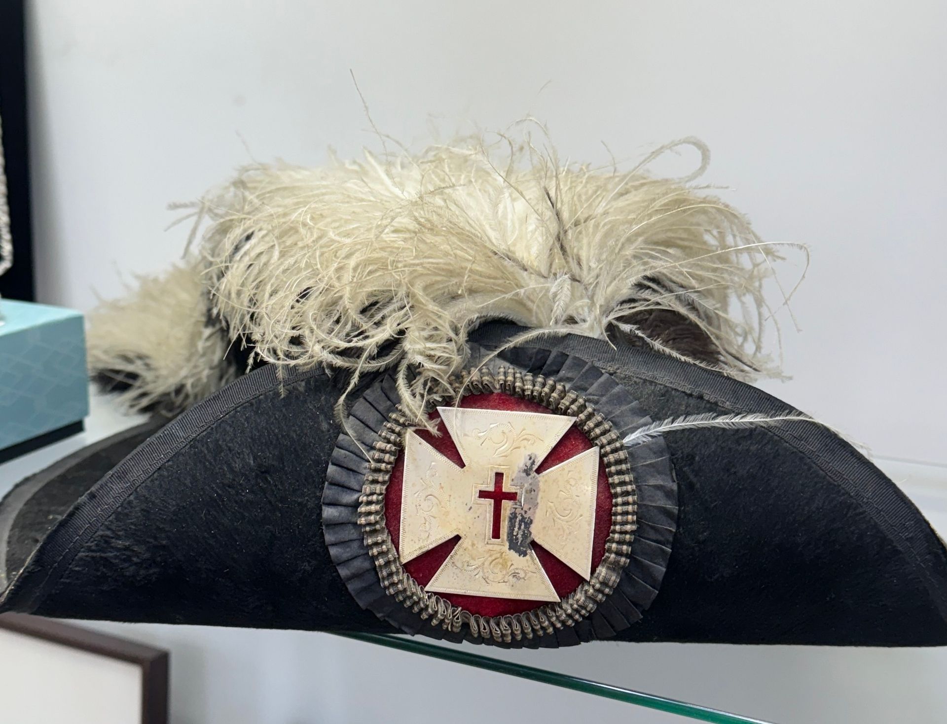 Black bicorne hat with white feather plume and red-and-white badge on the front