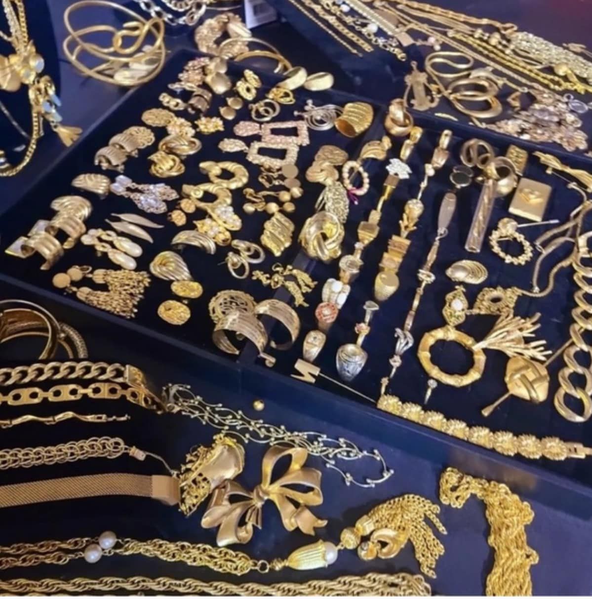 Assorted gold jewelry pieces displayed on dark blue fabric, including necklaces, bracelets, rings, and earrings