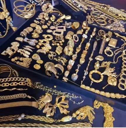 Assorted gold jewelry and trinkets arranged on a dark blue cloth display.