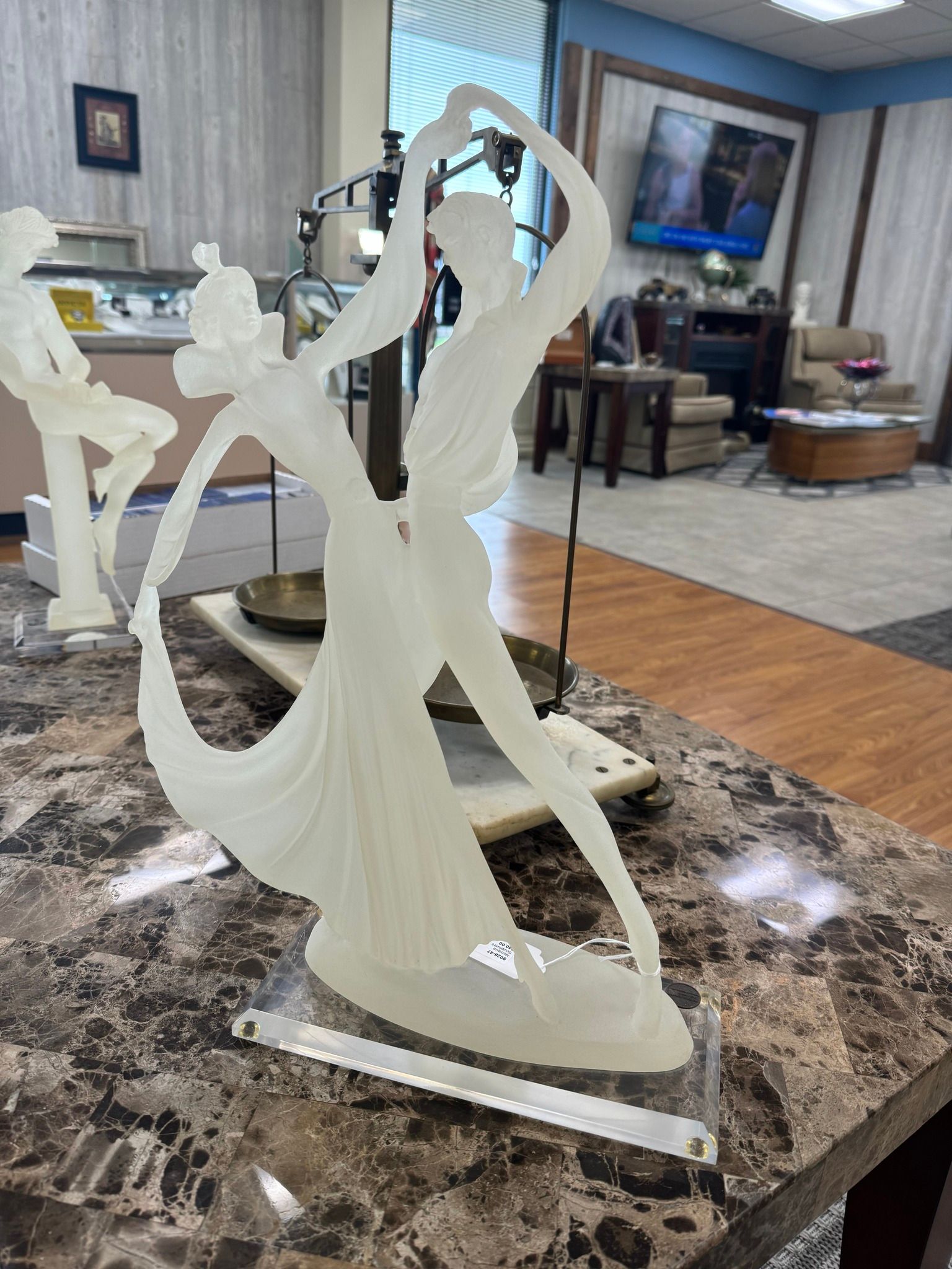 White abstract sculpture on a marble table in a living room, with a TV and sofa in the background