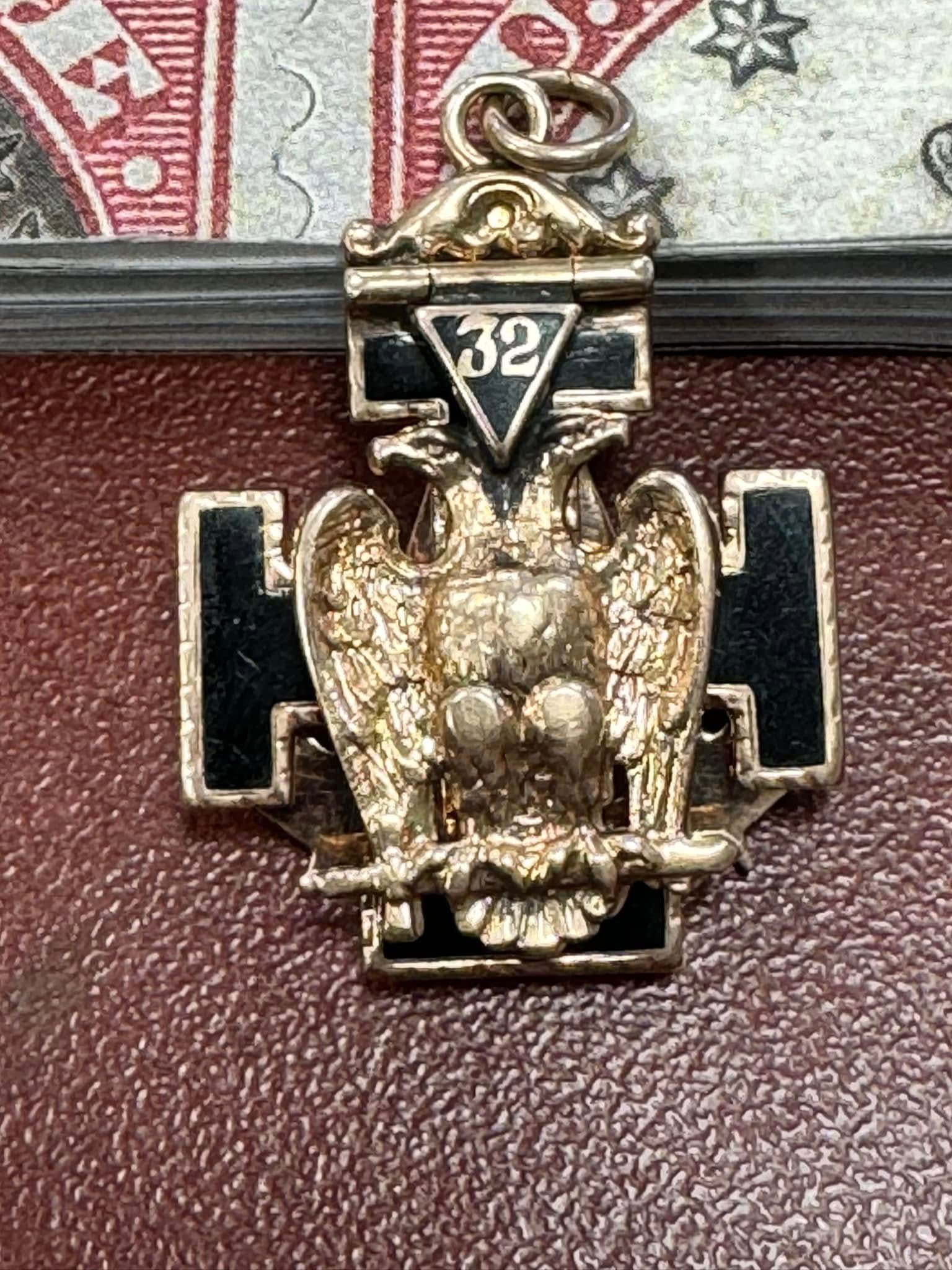 Gold eagle pendant with a black triangle marked “32” on a black-and-gold cross-shaped background