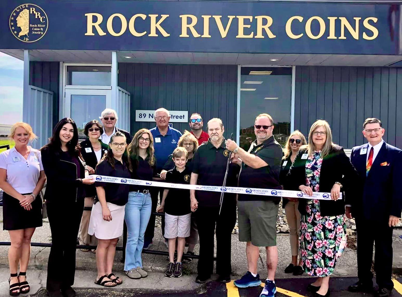 Group of people standing outside Rock River Coins, holding a giant ceremonial key at a ribbon cutting