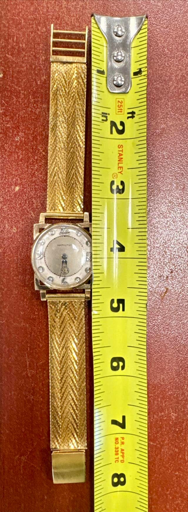 Silver watch beside yellow measuring tape on a red textured surface.
