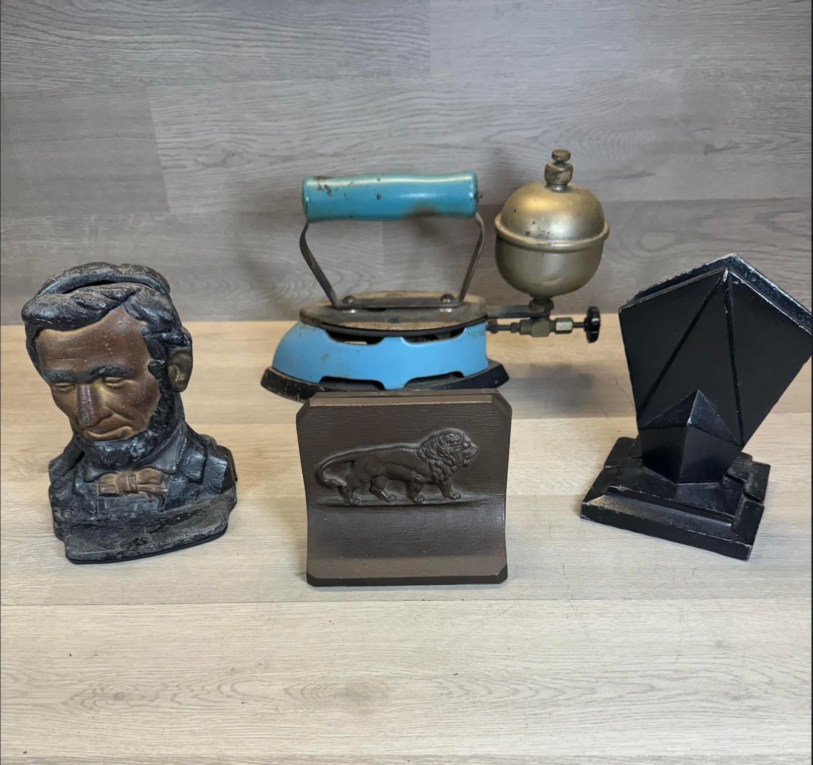 Three small decorative figurines on a gray surface, including a blue vintage iron and black geometric sculpture.