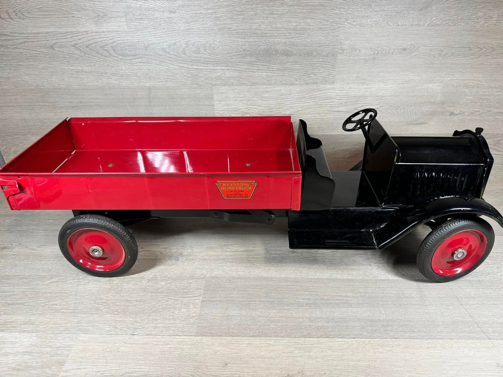 Red and black vintage toy truck with a red cargo bed on a light wood surface