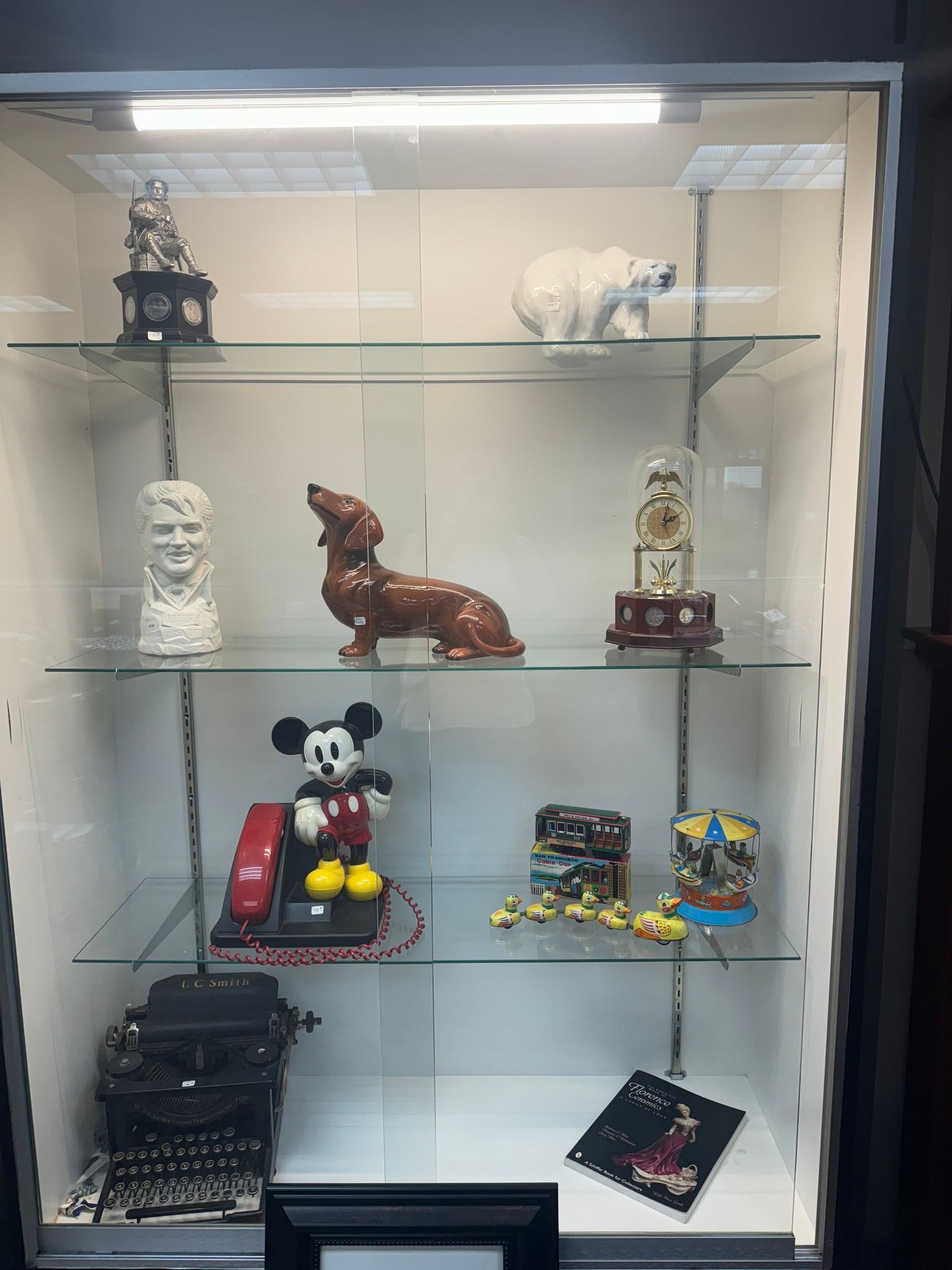 Glass display cabinet with assorted figurines, including a Mickey Mouse toy, decor, and small collectibles