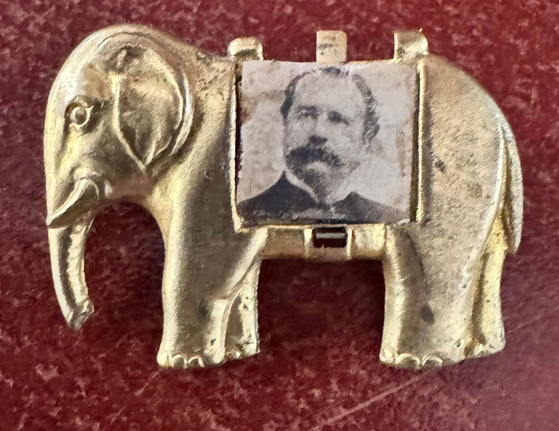 Small gold elephant brooch with a black-and-white portrait inset on a red background