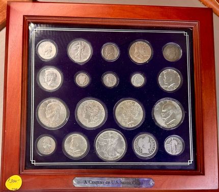 Framed display of silver coins arranged on a dark blue background in a wooden case