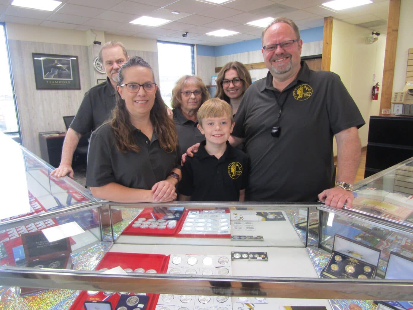 Five people posing behind a glass display case in a shop or museum, smiling at the camera.
