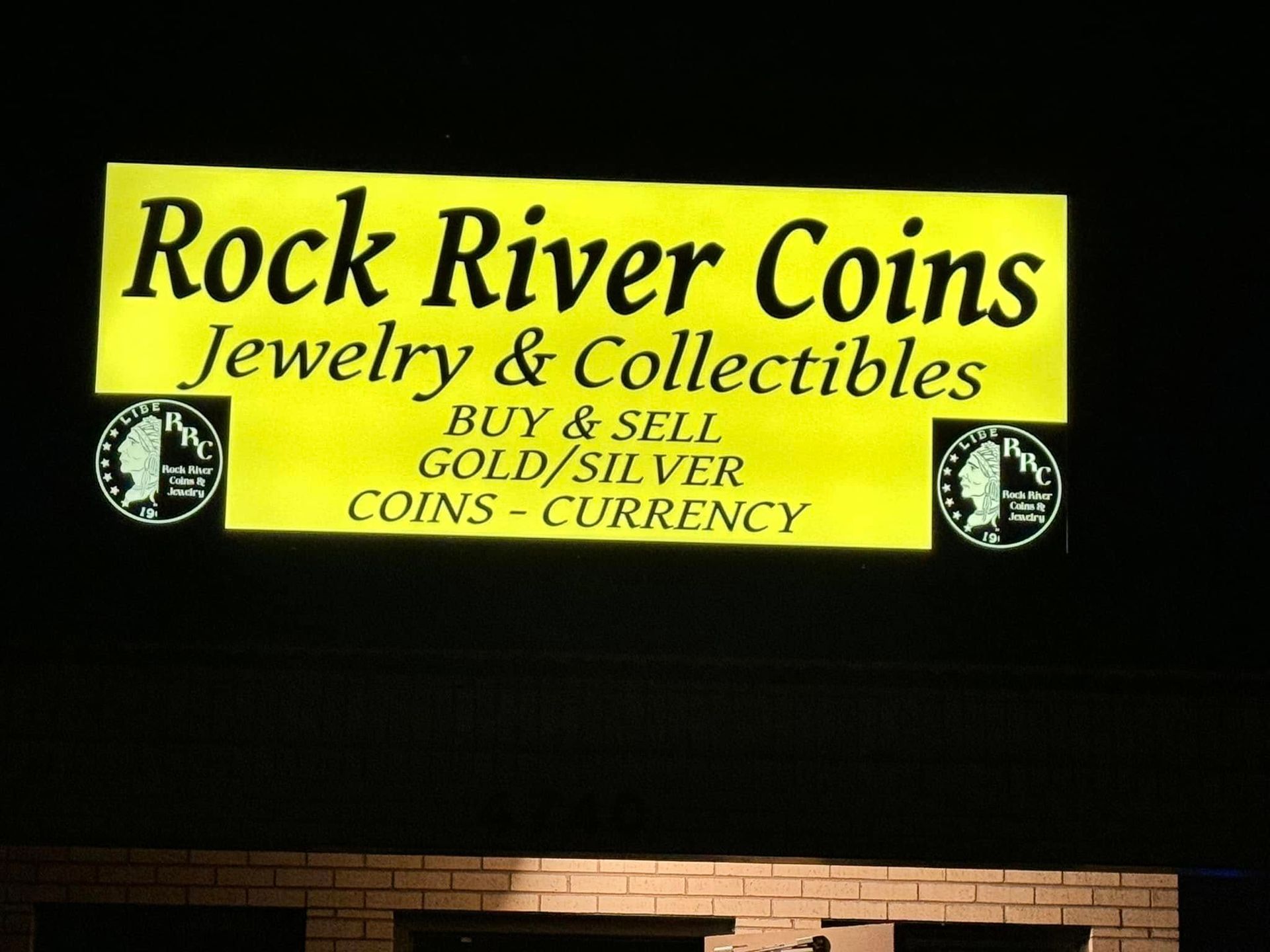 Rock River Coins sign on a black background with yellow lettering, advertising jewelry and collectibles.