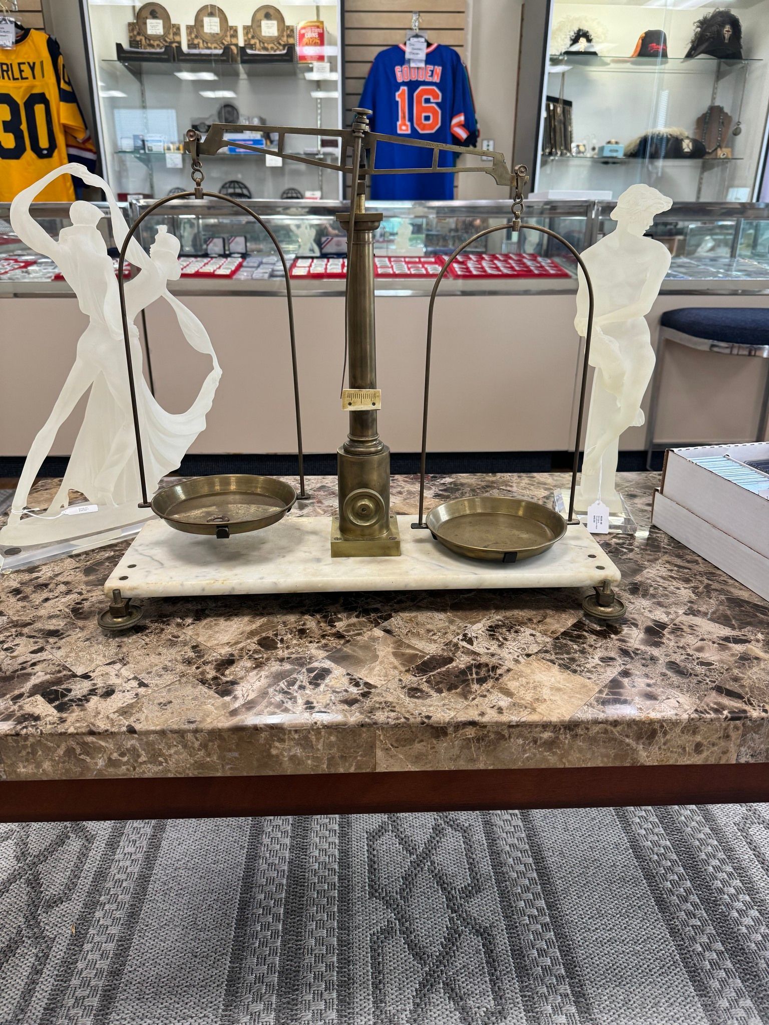 Brass balance scale on a marble counter in a sports memorabilia store, flanked by white horse figures.