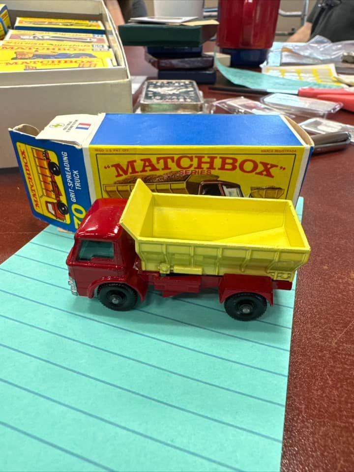 Red-and-yellow Matchbox toy truck on a blue lined paper notebook, with its box behind it.