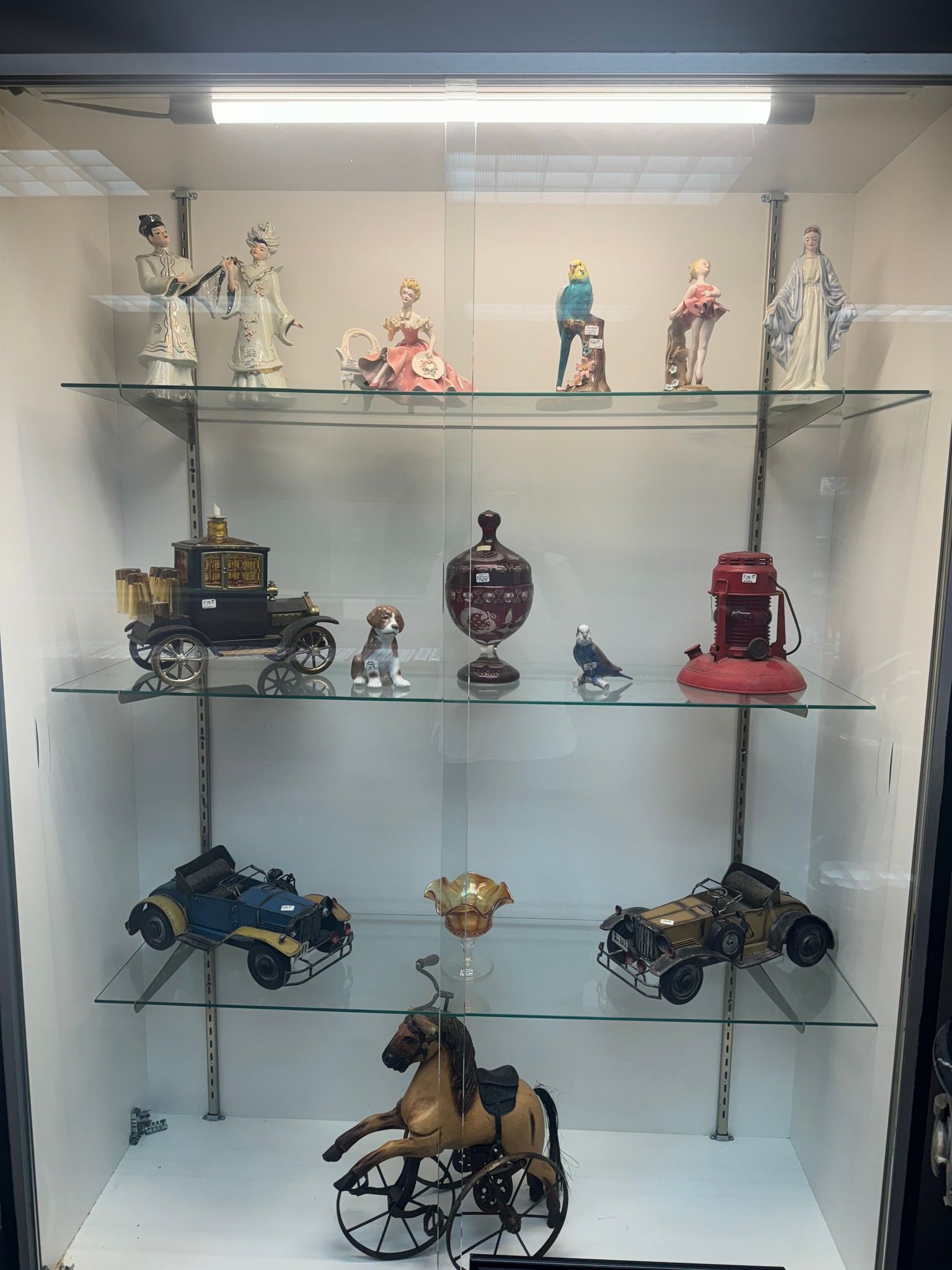 Glass display cabinet with assorted figurines, toy vehicles, and small collectibles on shelves