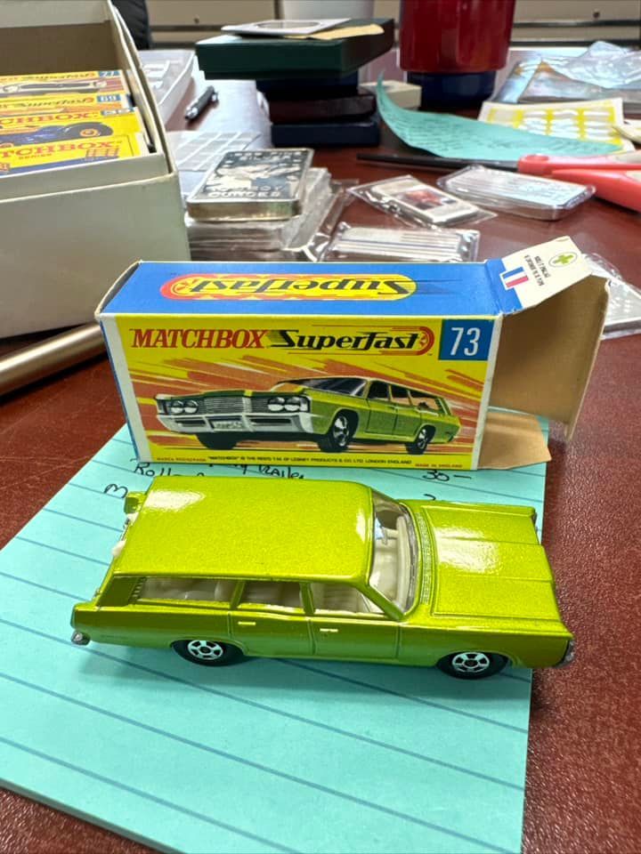 Yellow Matchbox Superfast toy car in its box on a desk, with a lime green toy car in front.