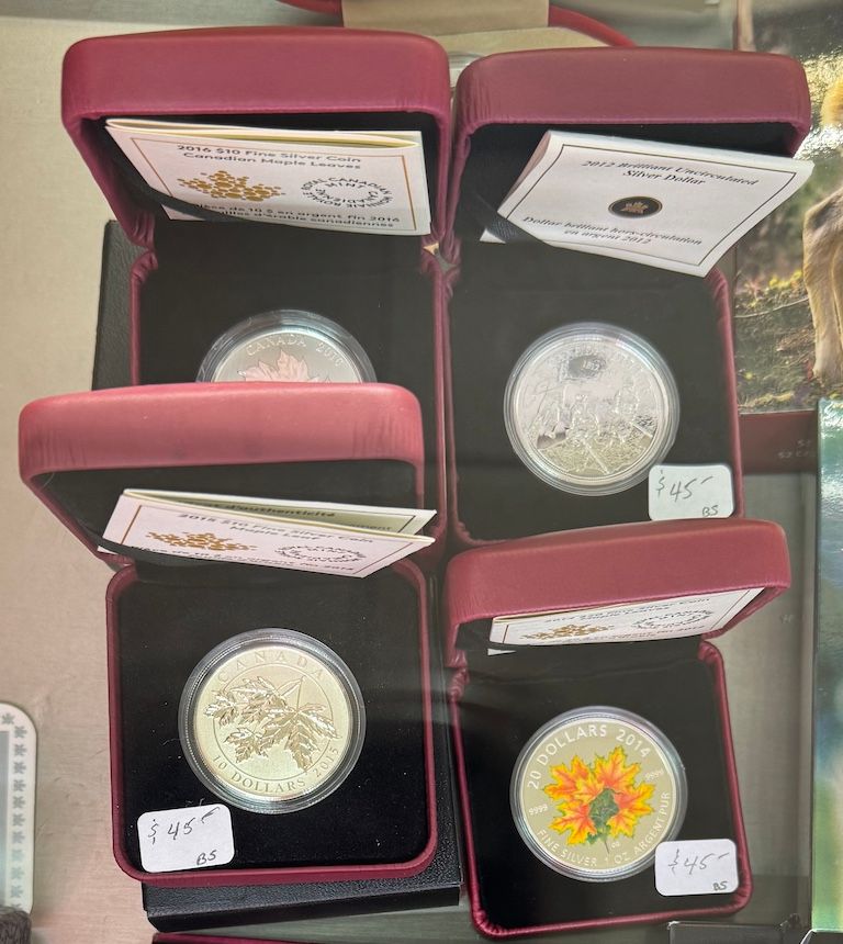 Four open coin cases with silver coins and colorful inserts on a tabletop.