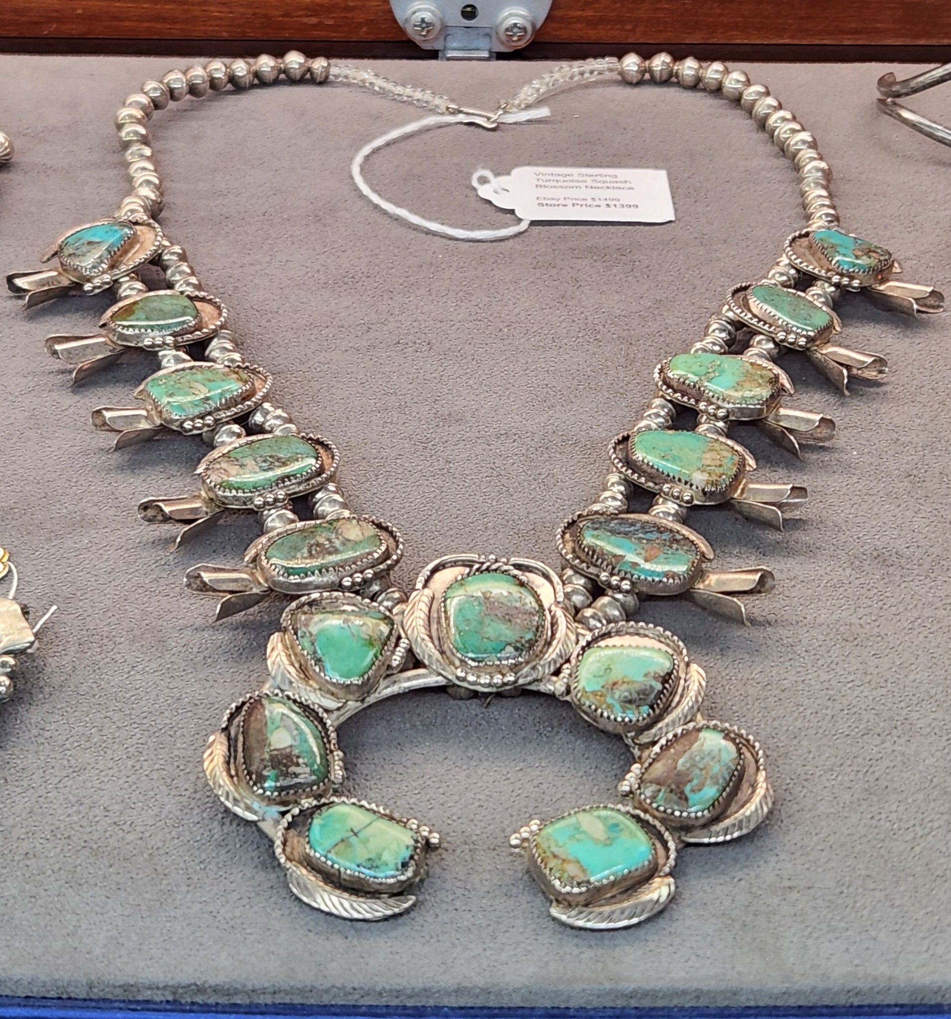 Turquoise and silver statement necklace displayed on a gray jewelry tray