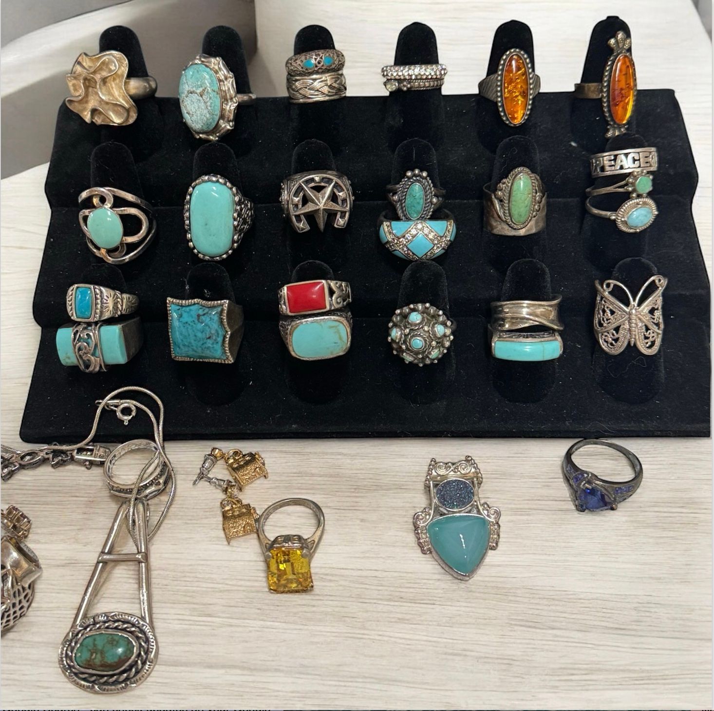 Assorted turquoise and silver rings and necklaces displayed on a black stand and white surface.